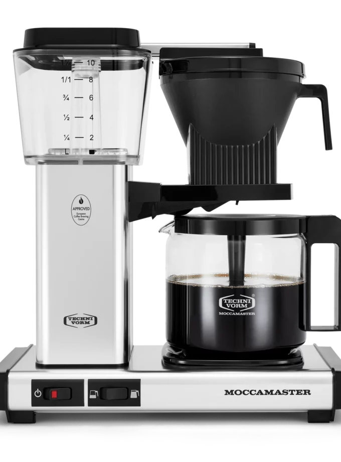 Front shot showing Moccamaster KBGV Select in Polished Silver, with rectangular tower and base, clear acrylic water reservoir with fill level marks, power and volume selector switch, glass carafe with black handle, and black automatic brew basket.