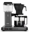 Front shot showing Moccamaster KBGV Select in Stone Grey, with rectangular tower and base, clear acrylic water reservoir with fill level marks, power and volume selector switch, glass carafe with black handle, and black automatic brew basket.